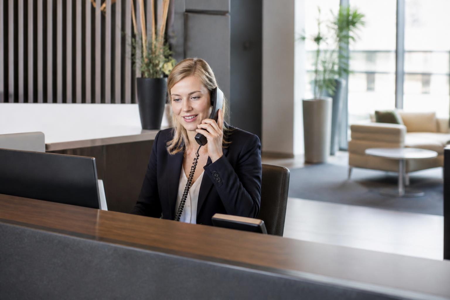 A professional receptionist answering a business phone in a modern office.
