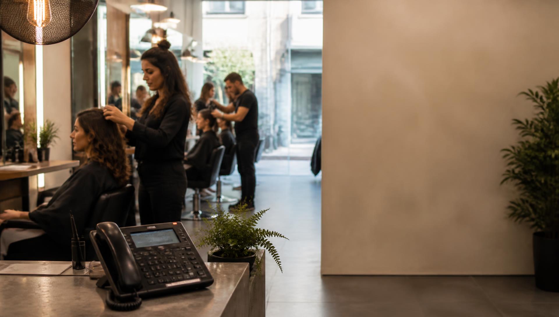 A stylist serving a customer in a busy salon while the reception phone rings.